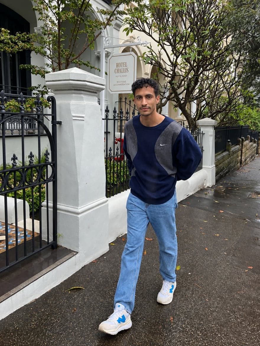 Man in a navy sweatshirt and light jeans walking past a boutique hotel gate