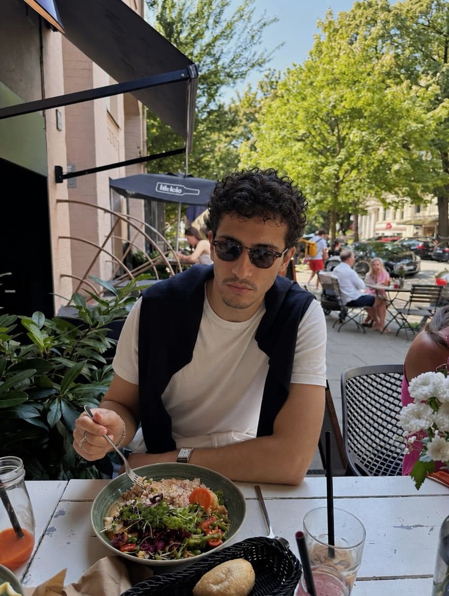 Man in sunglasses and a white T-shirt eating lunch on a café terrace