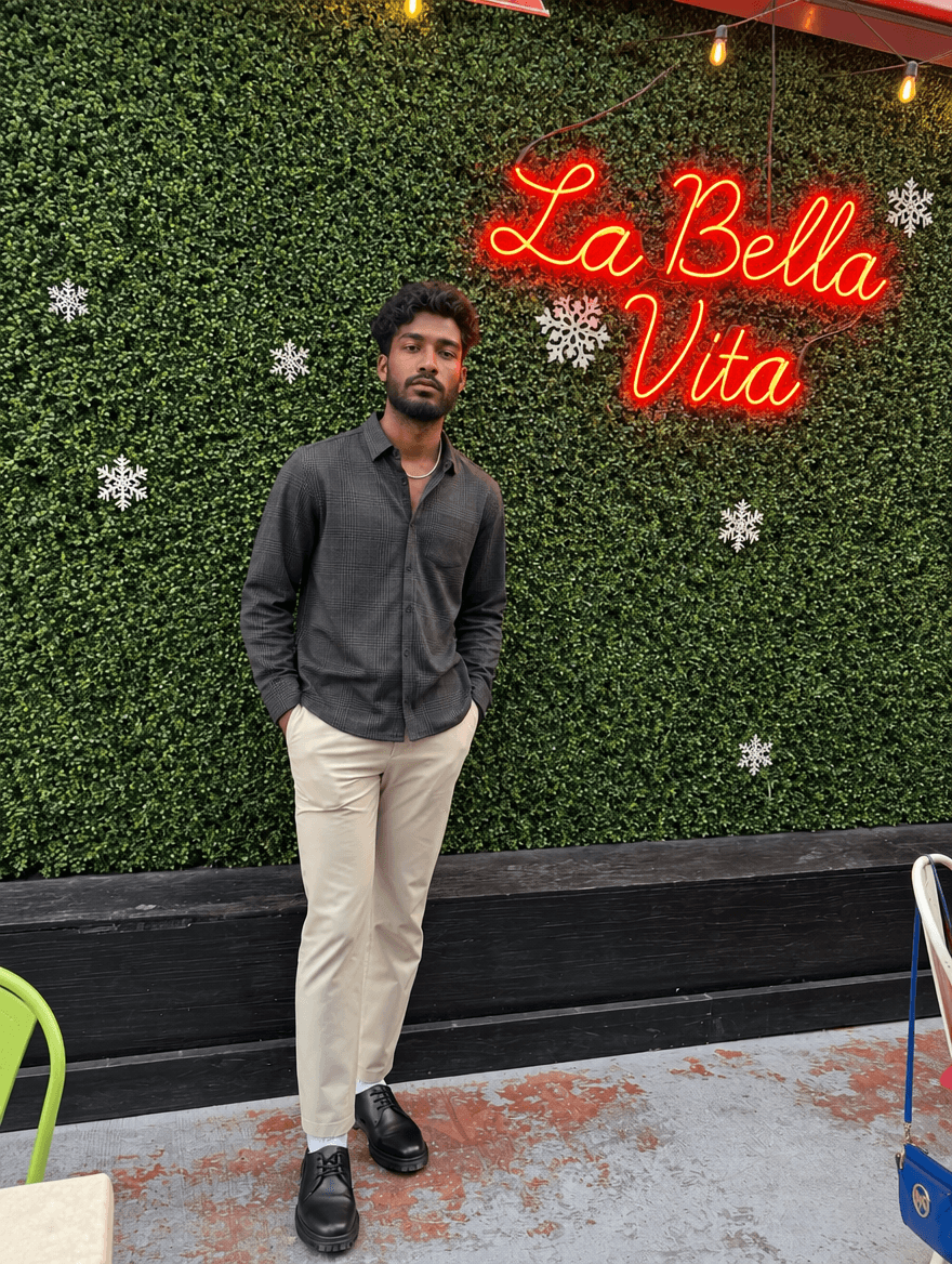 Man in a dark shirt and chinos standing by a neon sign on a green wall