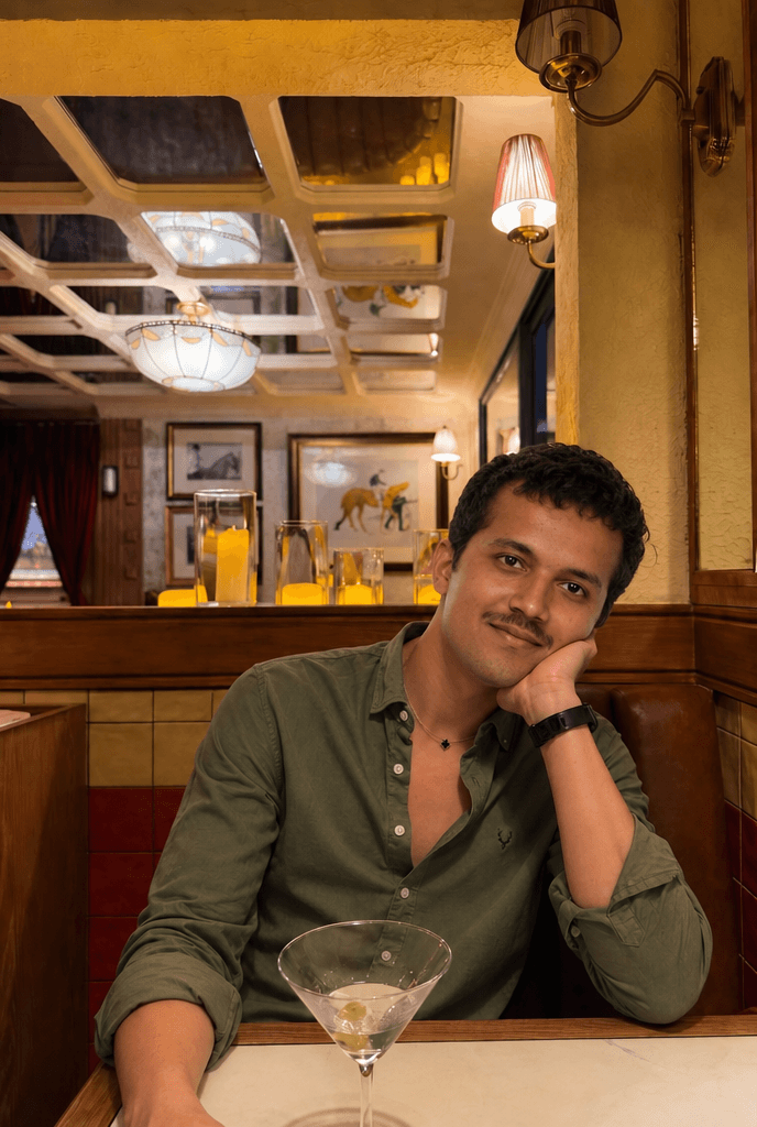 Man in an olive shirt smiling in a restaurant booth with a martini